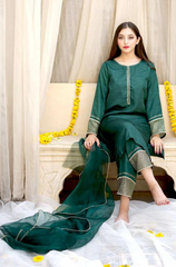 A woman in a green dress is seated gracefully on a bed, exuding elegance and tranquility in her surroundings.