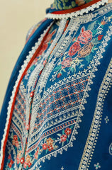 A woman in a blue and red dress adorned with floral embroidery, standing gracefully against a neutral background.