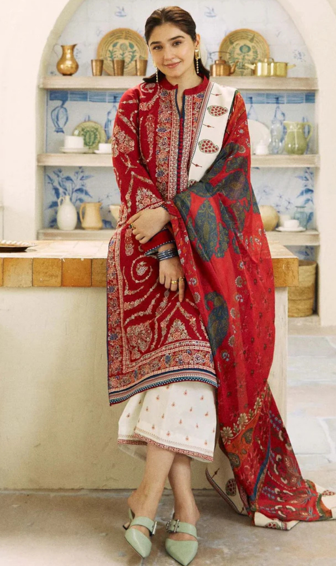 A woman dressed in red and white stands confidently on a counter, showcasing her vibrant outfit and poised demeanor.