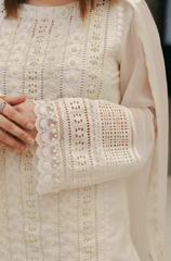 A woman in a white dress poses elegantly for a photo, smiling softly against a neutral background.