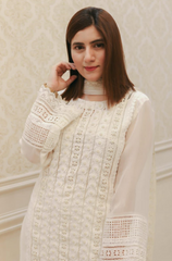 A woman in a white dress poses elegantly for a photo, smiling softly against a neutral background.